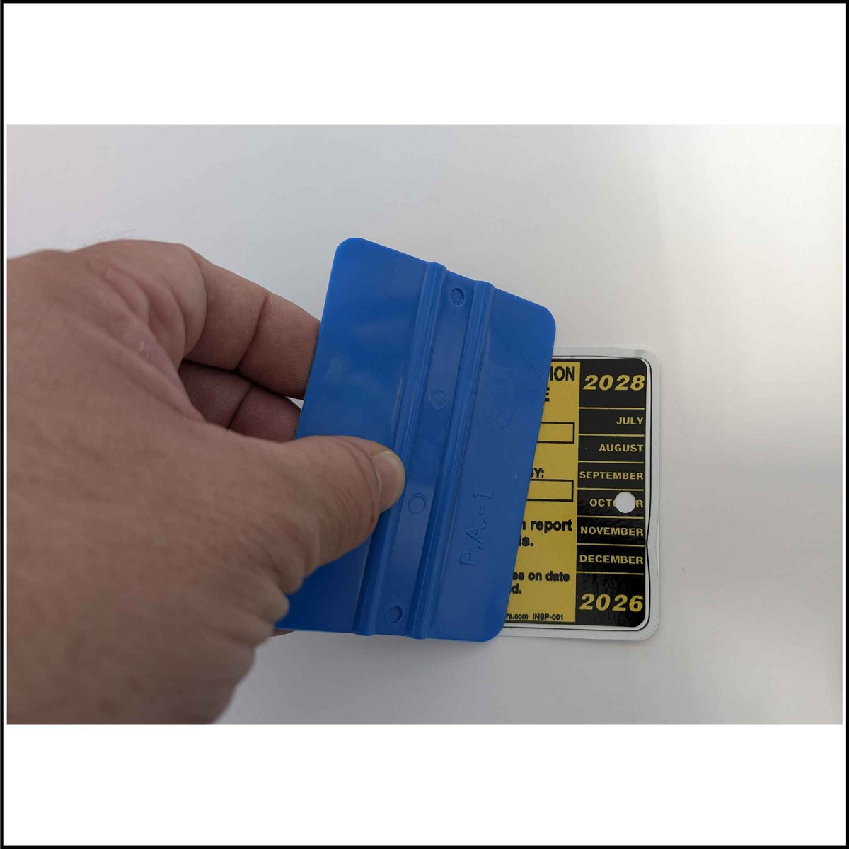 Hand using a blue squeegee to apply an inspection sticker.